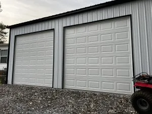 A pair of white short-panel residential garage doors on a metal-sided outbuilding