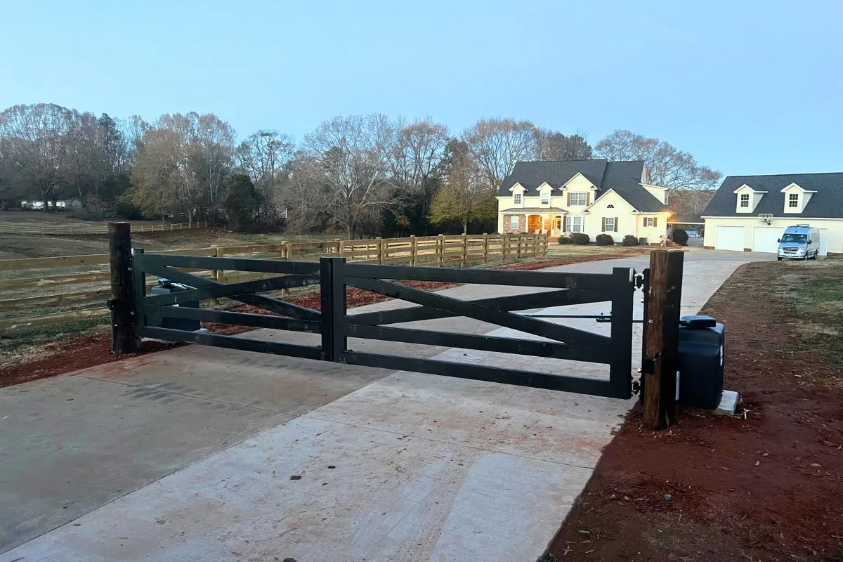 Black wood ranch-style double driveway gate fitted with automatic swing gate operators and a control box beside the concrete drive