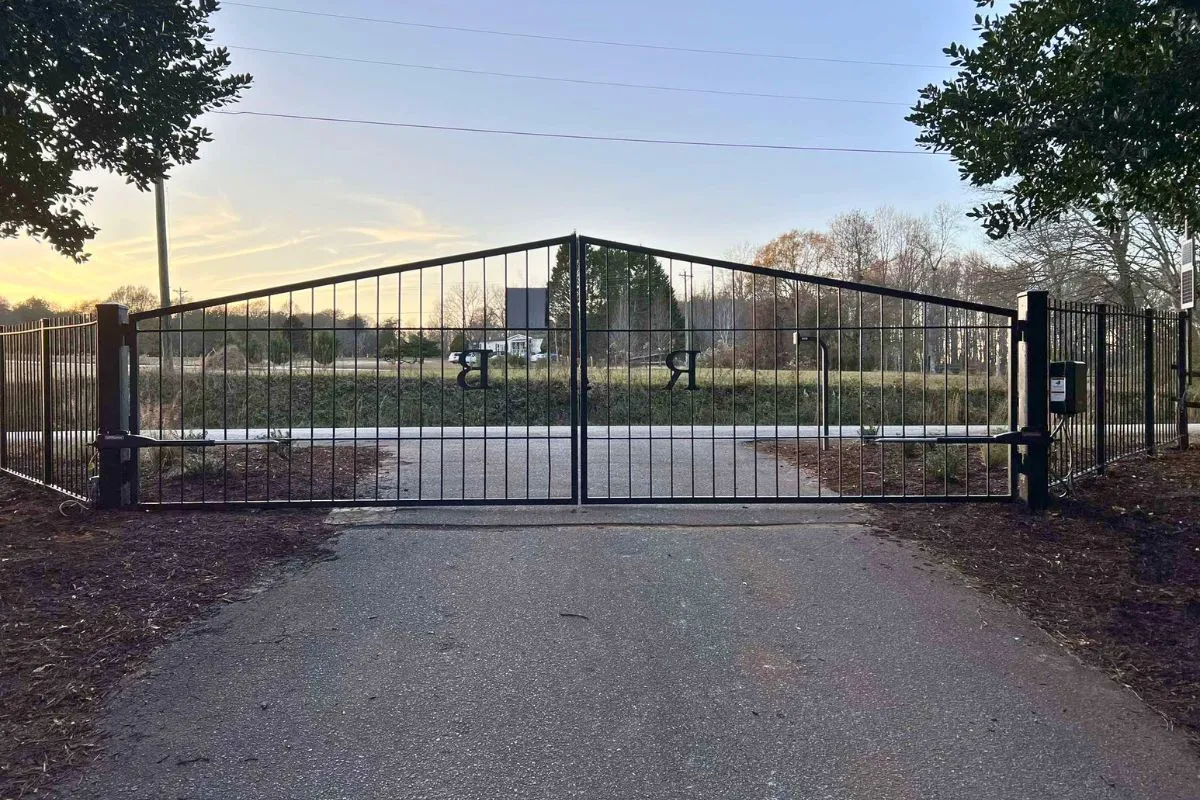 Tall ornamental metal double driveway gate with a peaked top, automatic operators on each leaf and a keypad control box at the entry