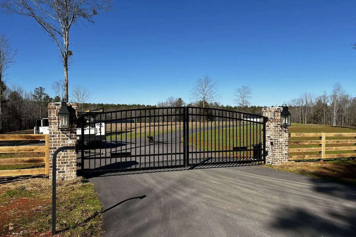 Arched ornamental driveway gate between brick columns on a rural Upstate South Carolina property, with a Door Tech service truck on site